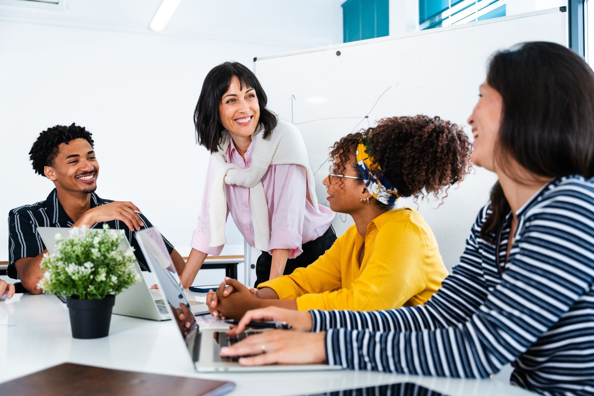 Coworkers in a bright office meeting around a laptop, talking and smiling