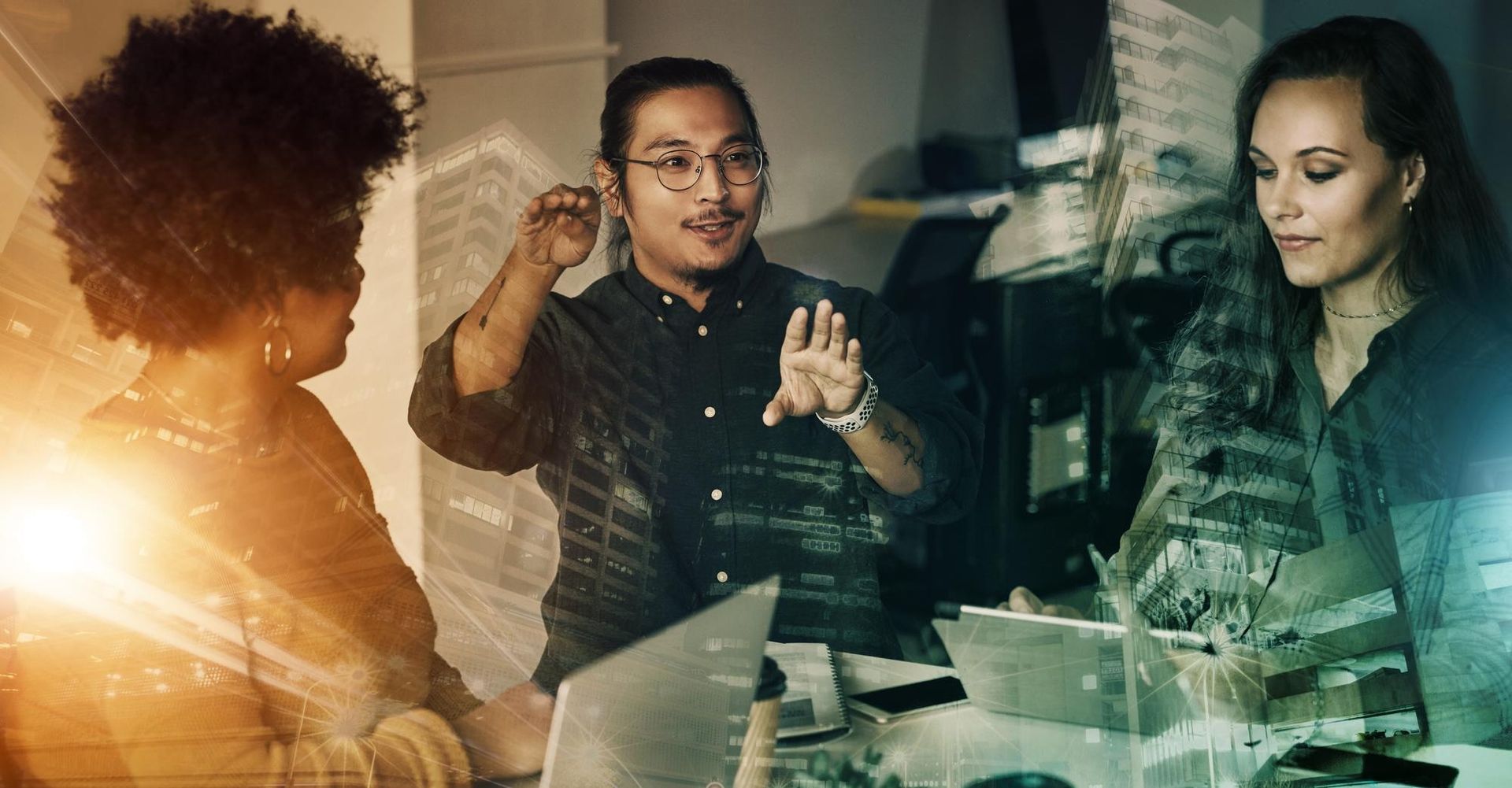 Three coworkers discussing ideas around a laptop in a sunlit office meeting room