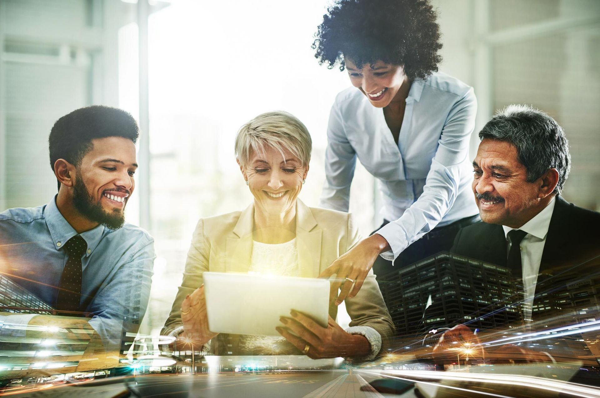 Four coworkers smiling around a laptop in a bright office, discussing work together