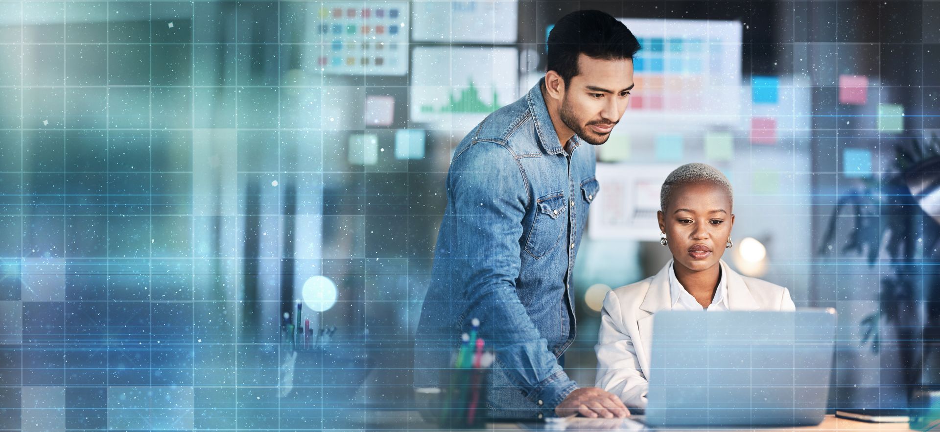 Two coworkers reviewing a laptop in a modern office with digital data graphics in the background