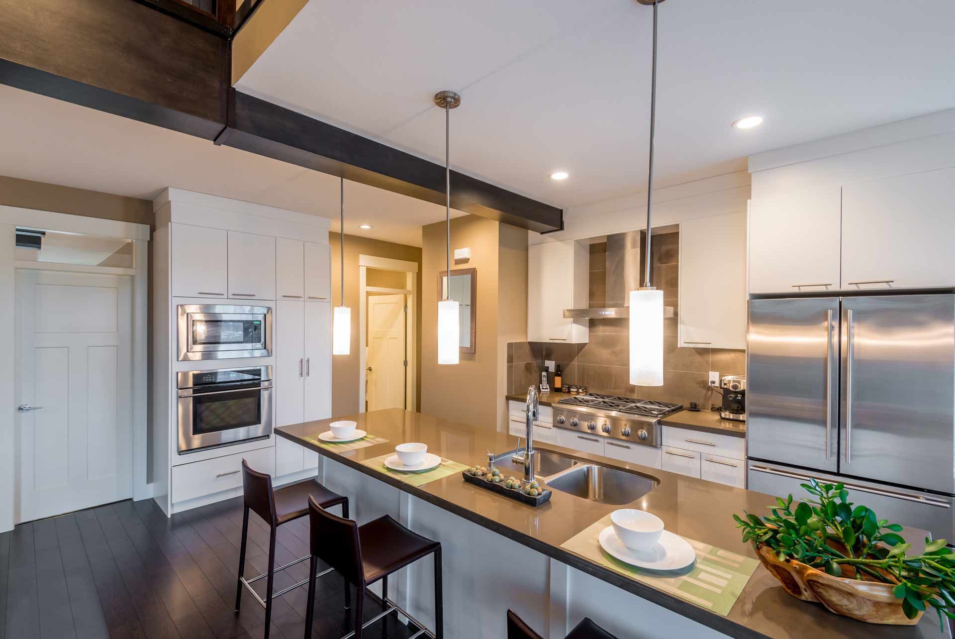 Modern kitchen with island, stainless steel appliances, white cabinets, dark wood floor.