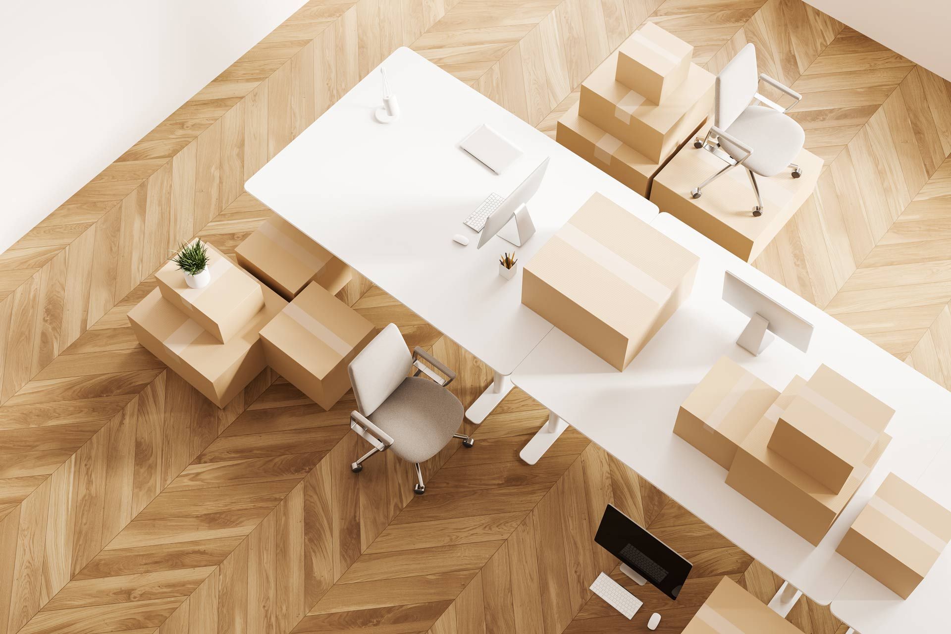 Office with long white desk, boxes, chairs, and computer monitors on a wooden floor.
