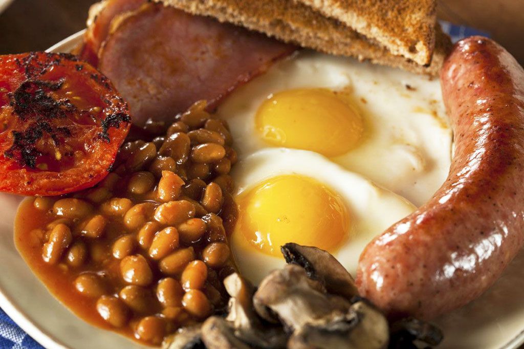 Full English breakfast: eggs, sausage, bacon, beans, tomato, mushrooms, and toast on a plate.