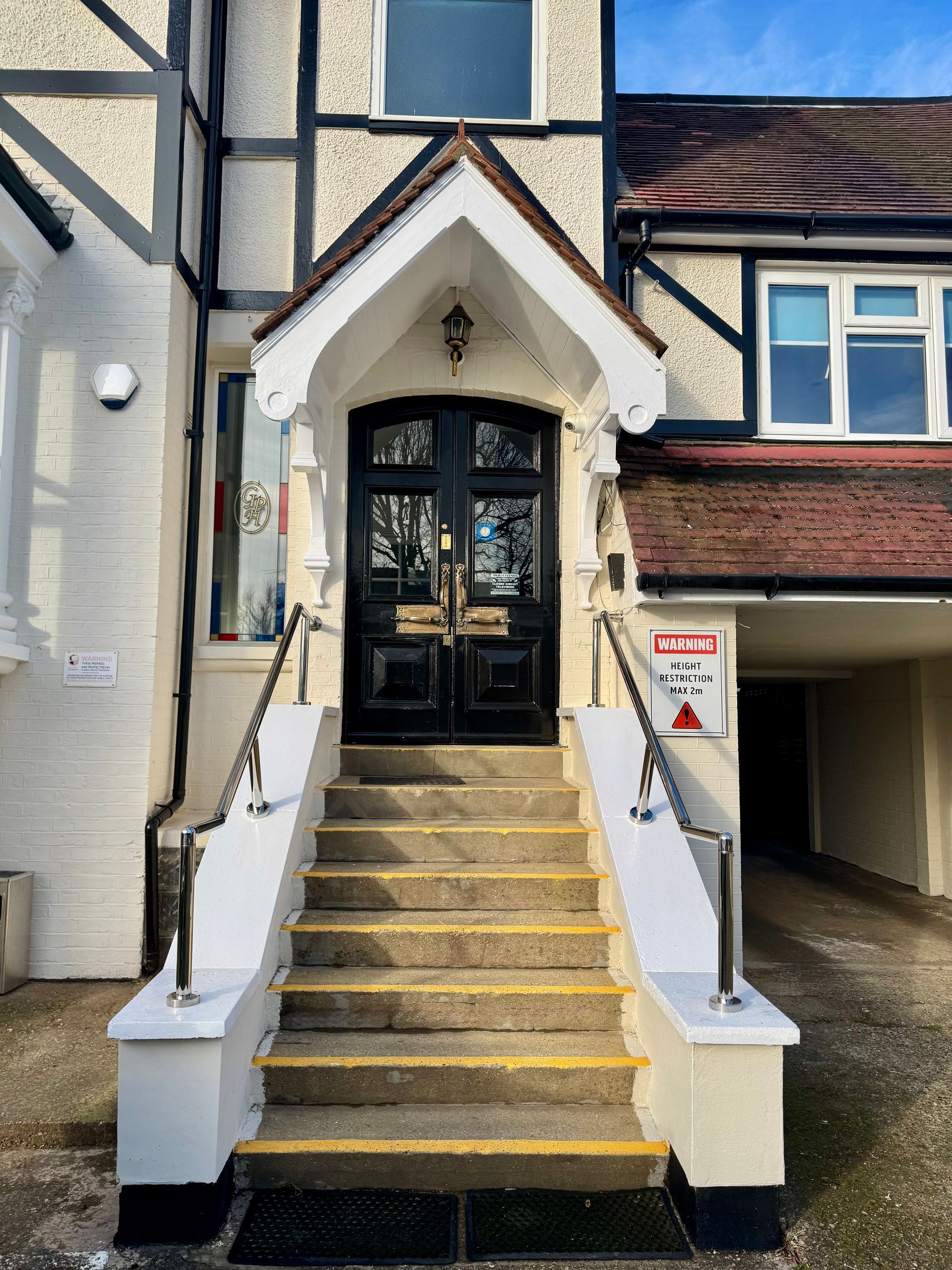 Stone steps lead to a black double door entrance with a white overhang. The building has a Tudor style.