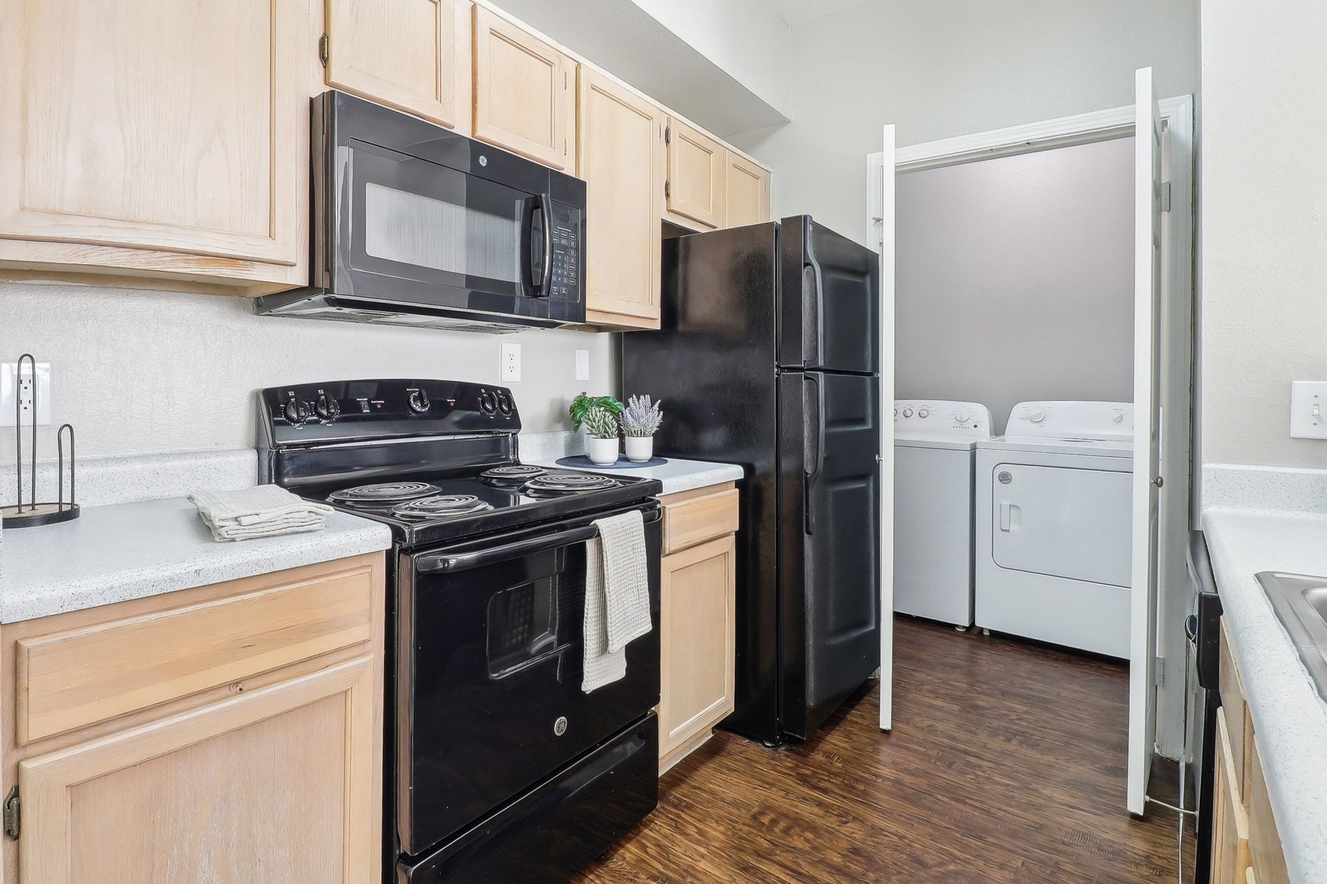 Kitchen with black appliances, beige cabinets, and laundry machines visible behind folding doors.