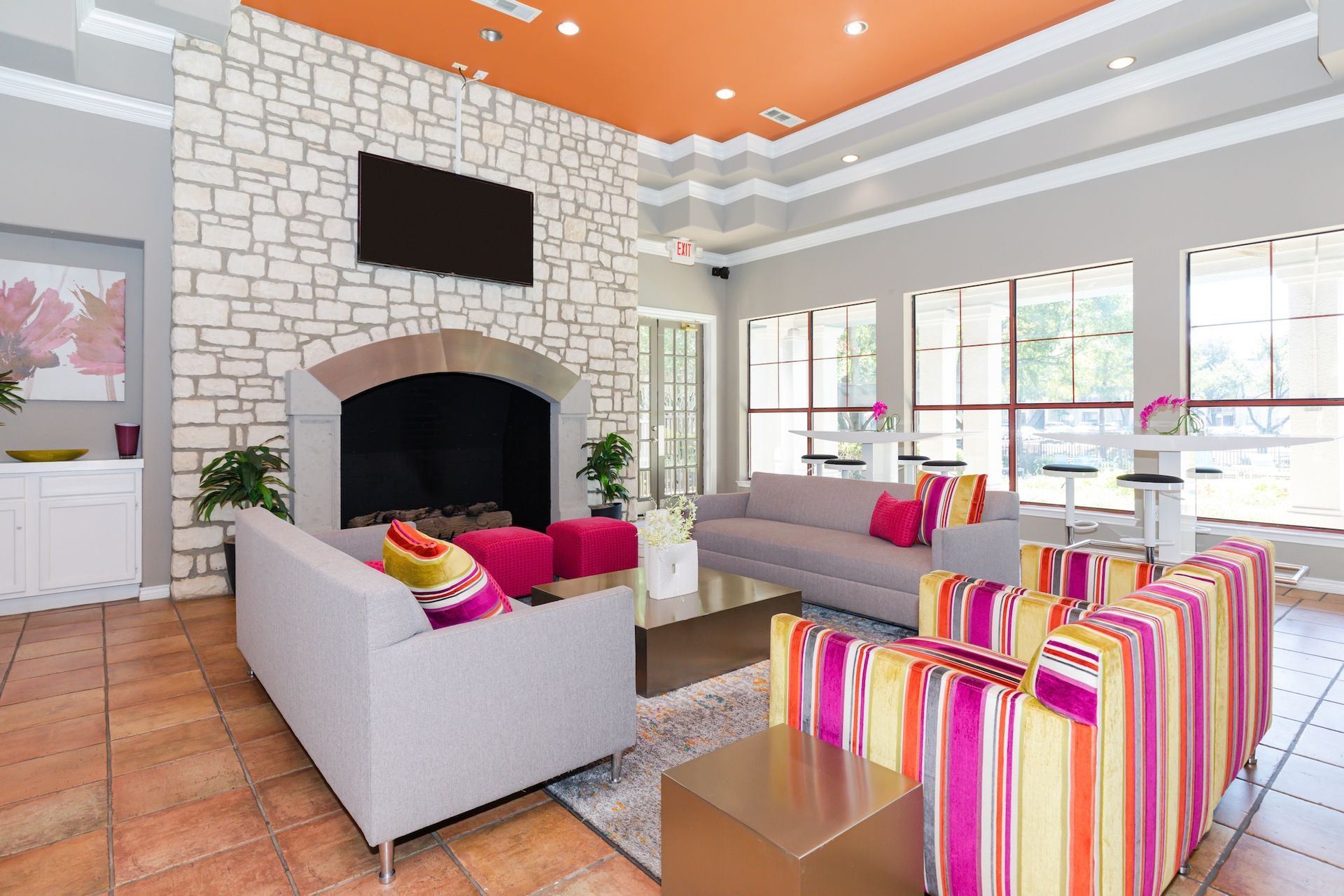 A modern living area with a stone fireplace, gray couches, and brightly colored striped armchairs under an orange ceiling.