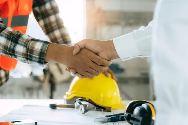 Two people shaking hands on a construction site; hard hat and tools in foreground.