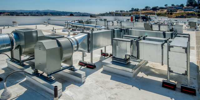 Rooftop HVAC units and ductwork on a flat commercial building with a city view in the distance