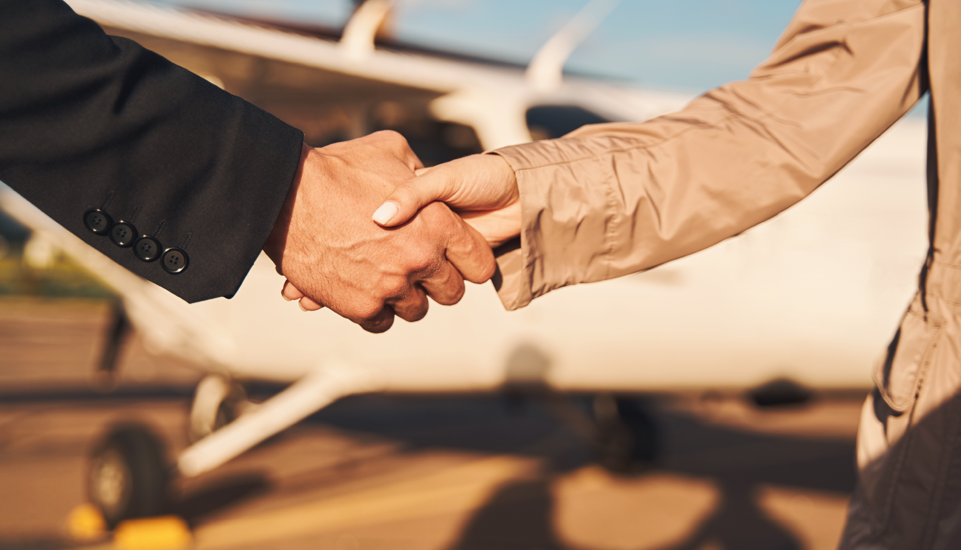 A man and a woman are shaking hands in front of an airplane.