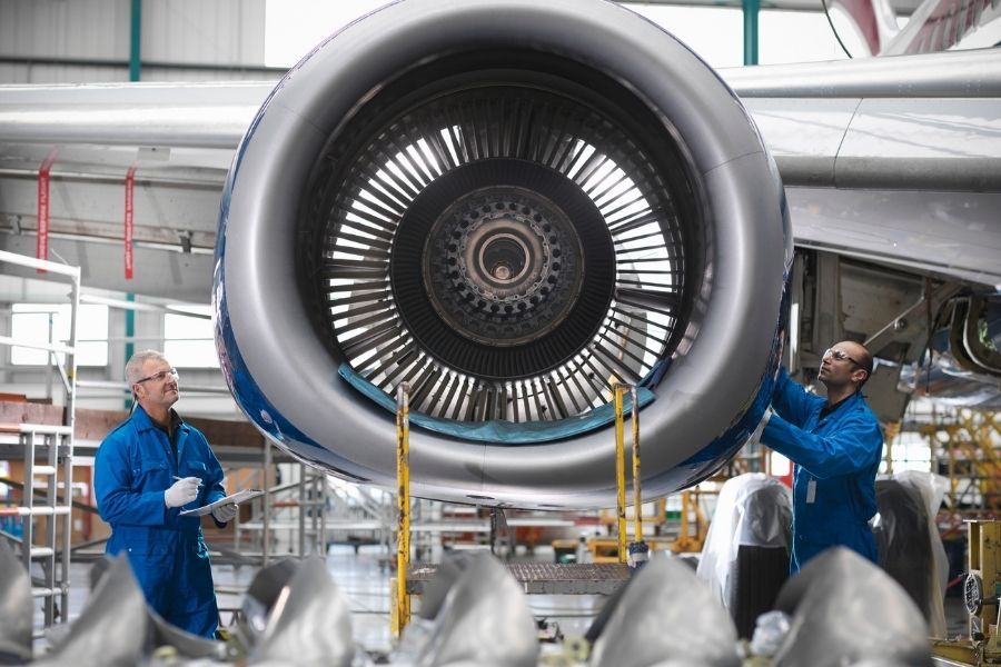 Two men are working on an airplane engine in a factory