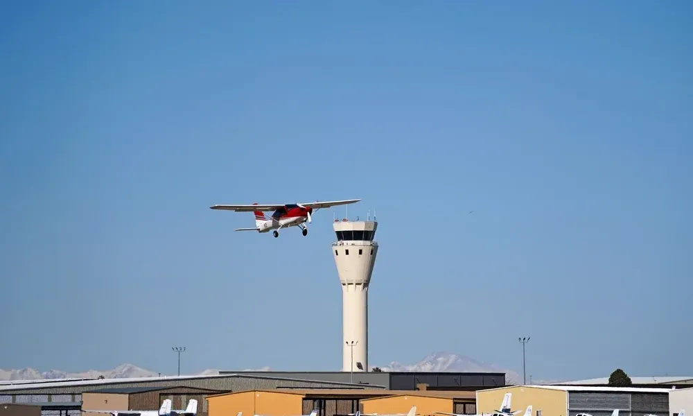 A plane is flying over an airport with a tower in the foreground.