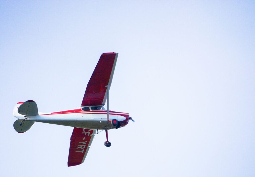 A small red and white plane is flying in the sky.