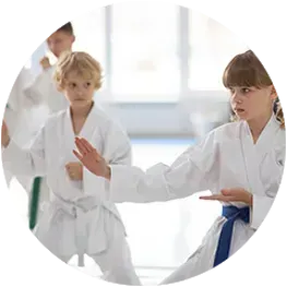 Students in white karate uniforms practicing martial arts moves in a bright studio.
