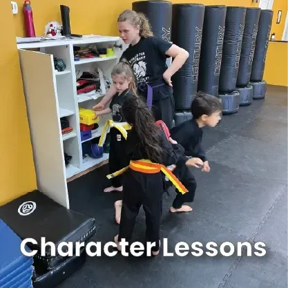 Four children in martial arts uniforms practice organized cleanup by a white storage shelf in a gym with standing bags.