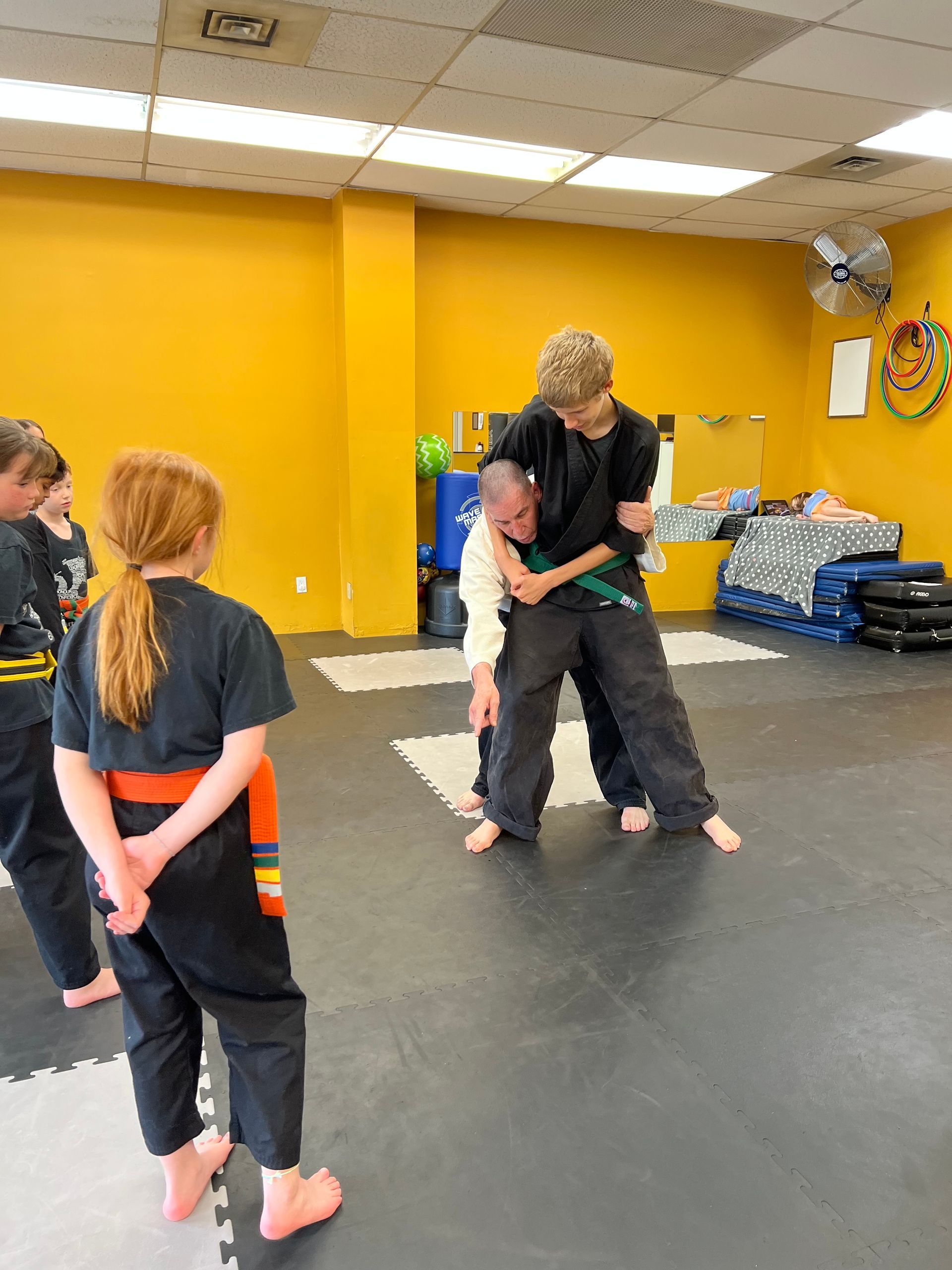 In a martial arts studio, a student performs a self-defense move on an instructor as two others watch.