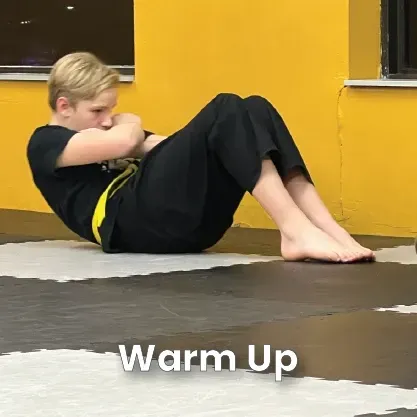 A person in a black martial arts uniform performing a sit-up on a gym mat during a warm-up.