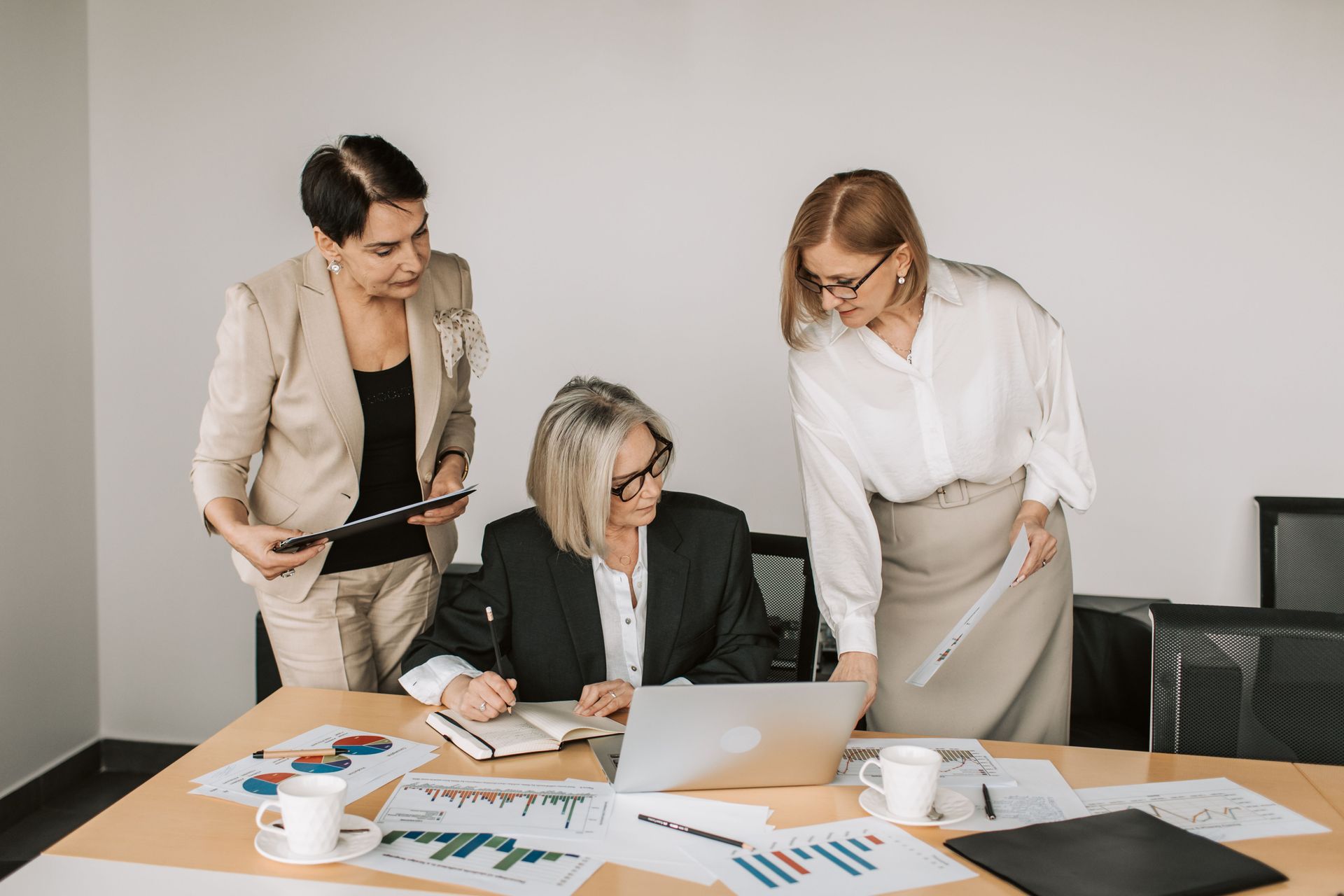 Three coworkers review charts around a laptop in a bright office meeting room.