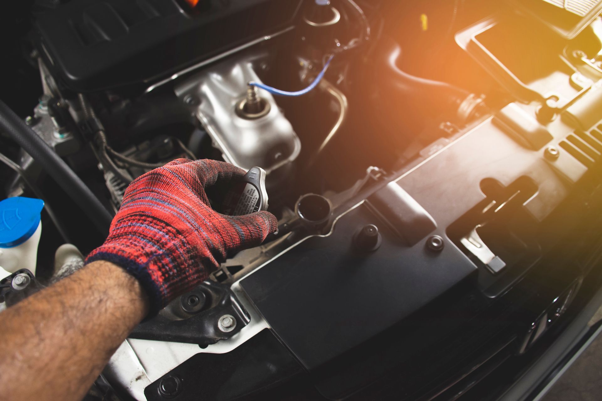 Gloved hand reaching into an open car engine bay, working on the engine.