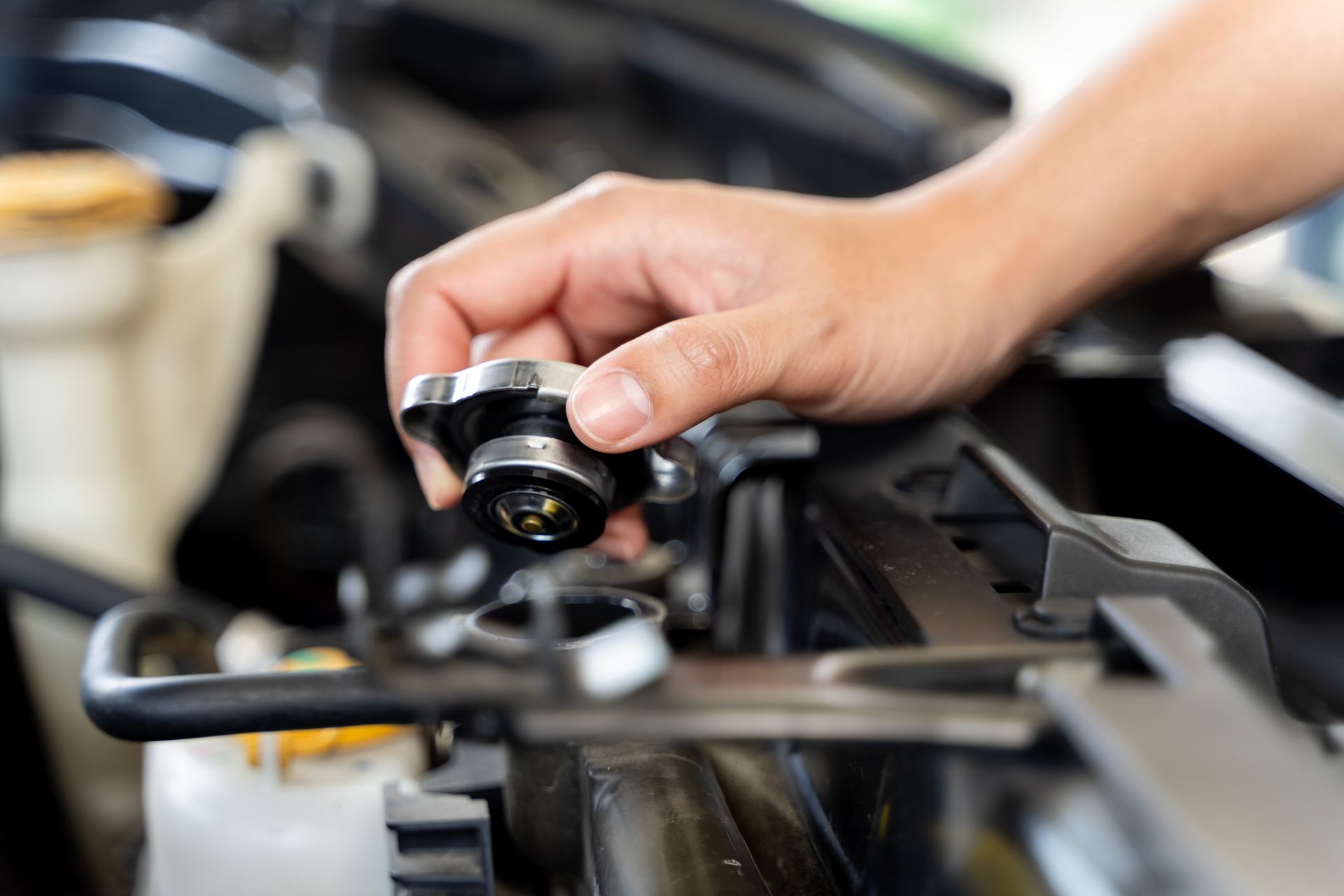 Hand removing a radiator cap from a car engine.