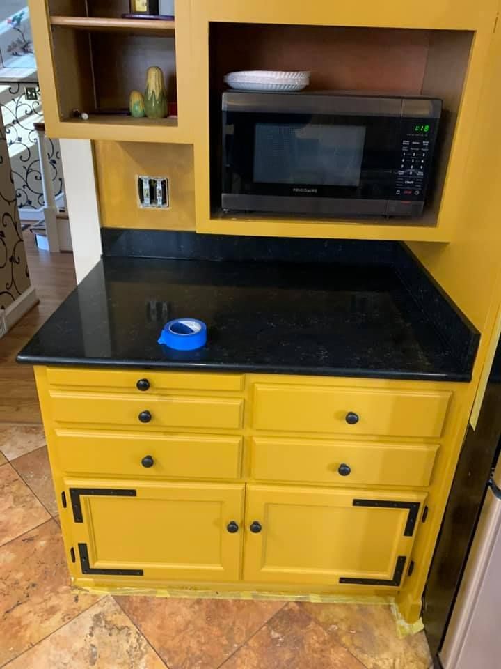 A yellow cabinet with a black counter top and a microwave on top of it.