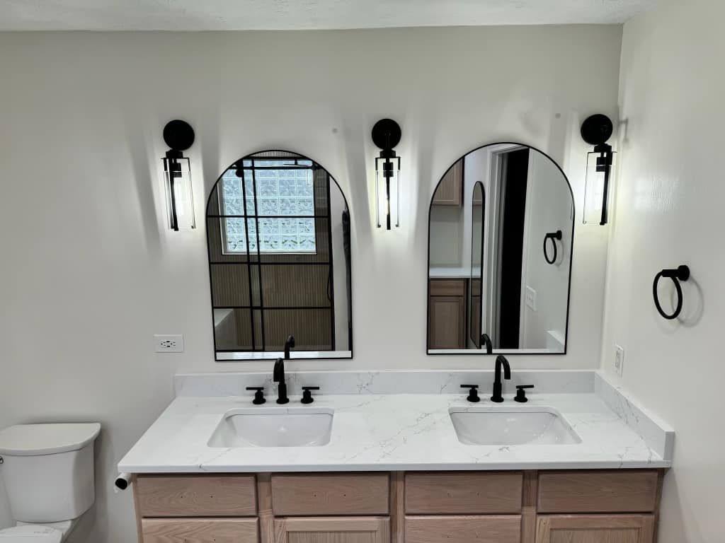 A bathroom with two sinks, two mirrors and a toilet.