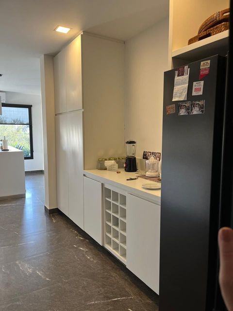 Cocina con gabinetes blancos, botellero, refrigerador negro, encimera con licuadora y vista de una isla de cocina.
