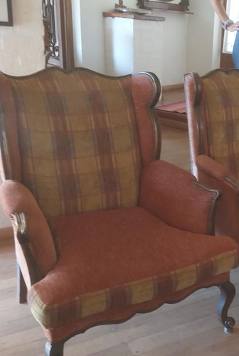 Sillón orejero tapizado en tela de cuadros, con una silla adyacente visible.