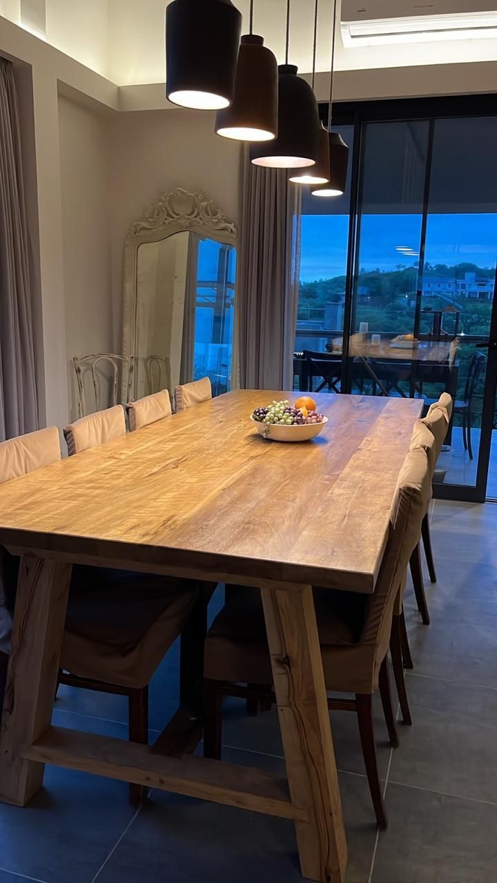 Juego de comedor largo de madera para muchas personas, con luces colgantes encima.