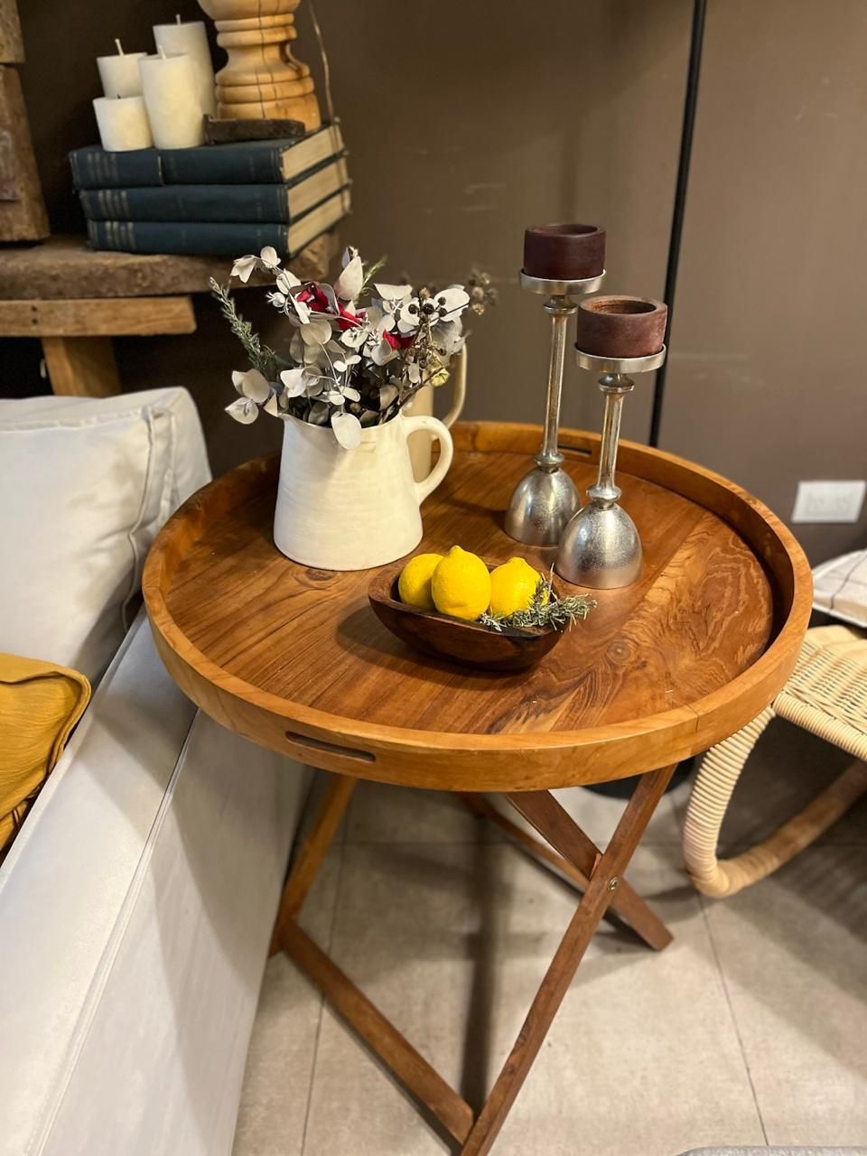 Mesa redonda de madera con bandeja, jarra de flores, limones y candelabros.