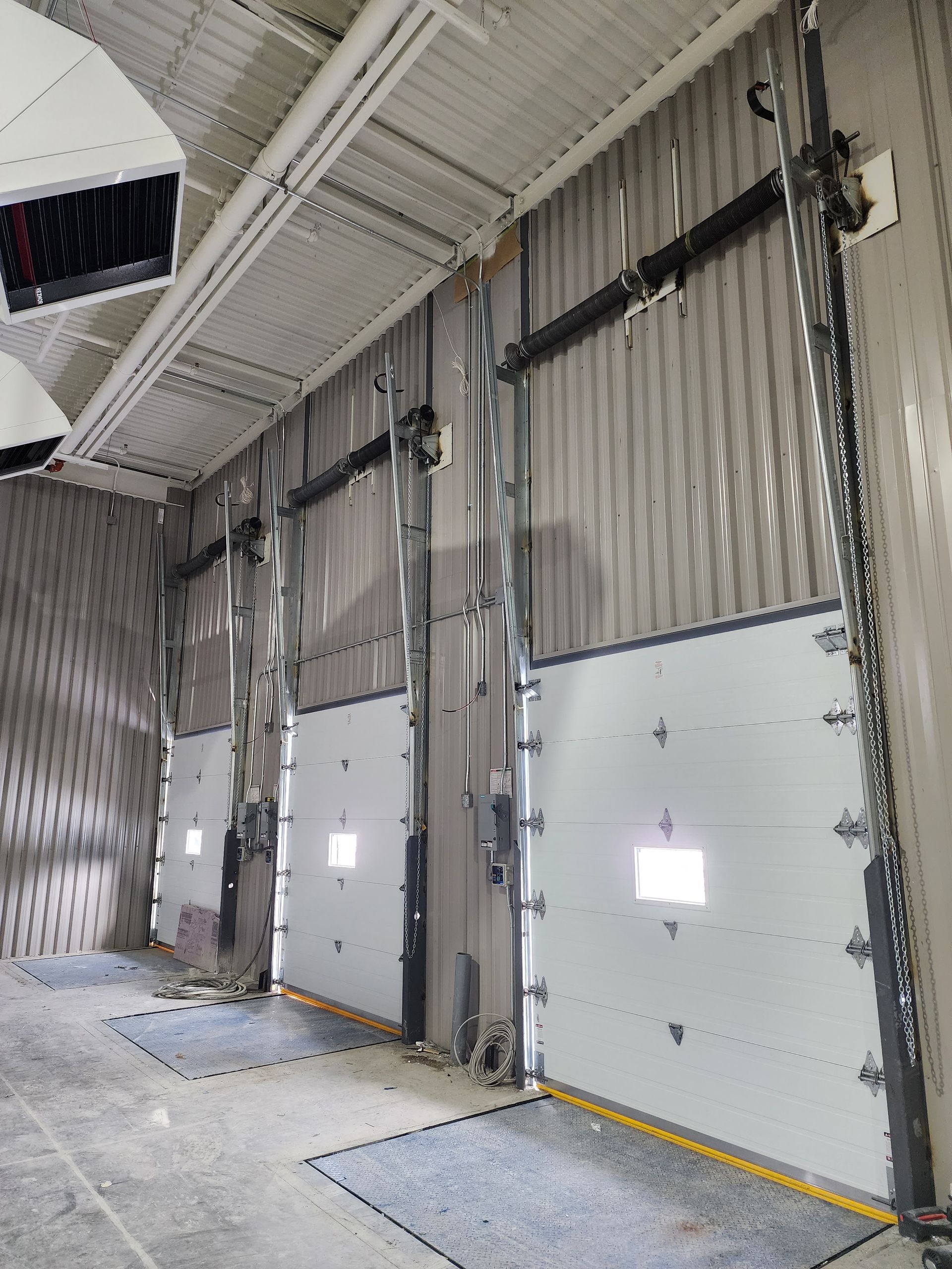 Deux portes de garage noires encastrées dans un bâtiment à l'extérieur sombre, le sol étant enneigé.