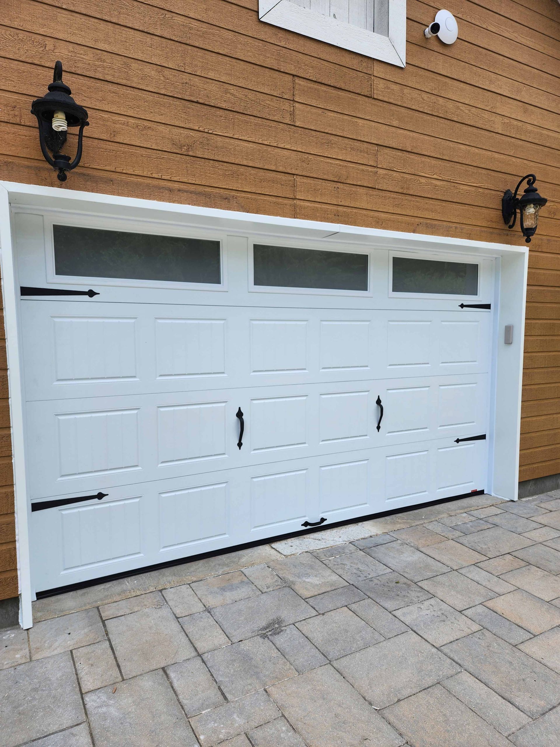 Une porte de garage blanche se trouve devant une maison brune.