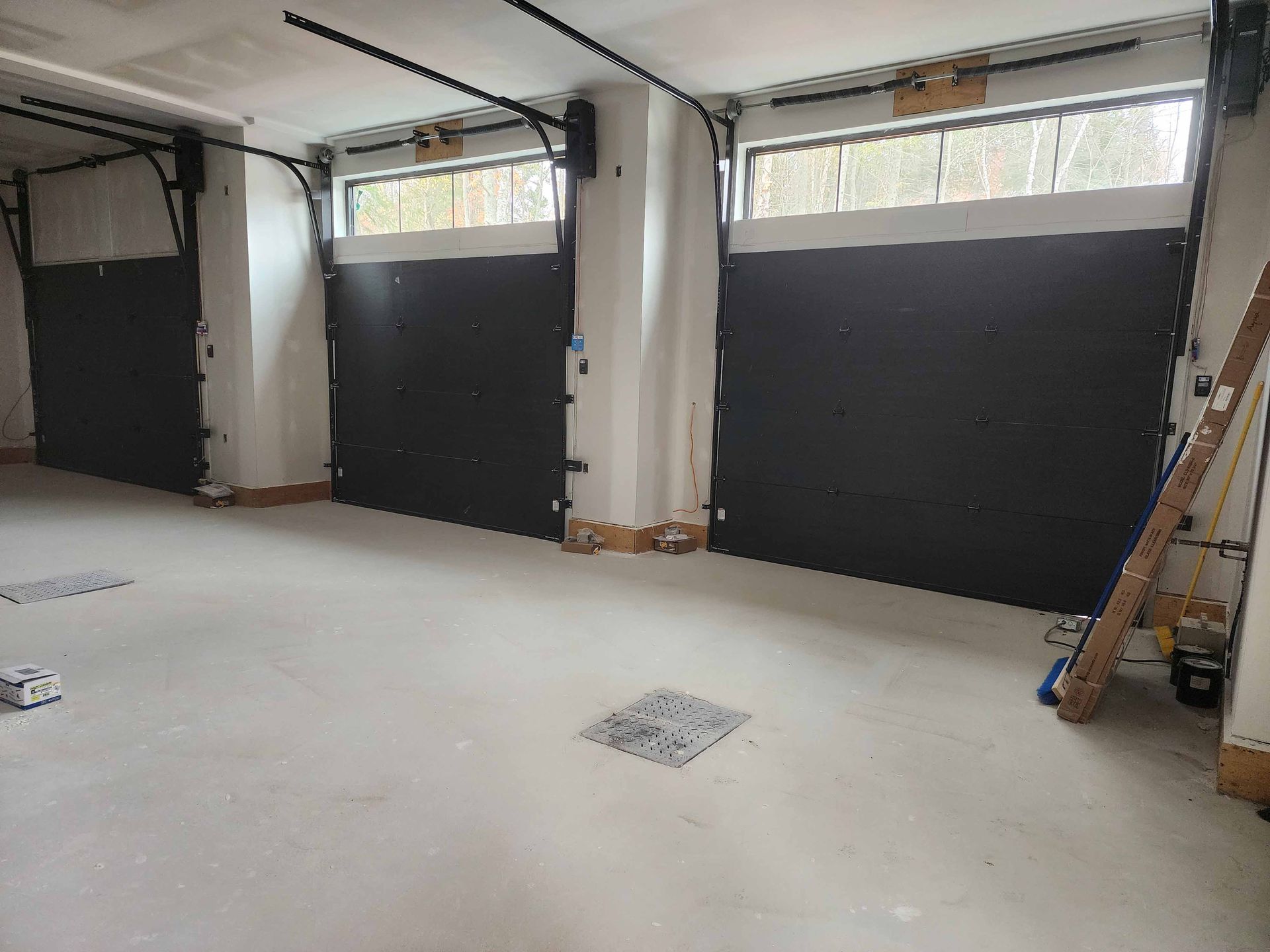 Trois portes de garage noires dans un intérieur clair. Chacune possède une petite fenêtre et un système d'ouverture visible.