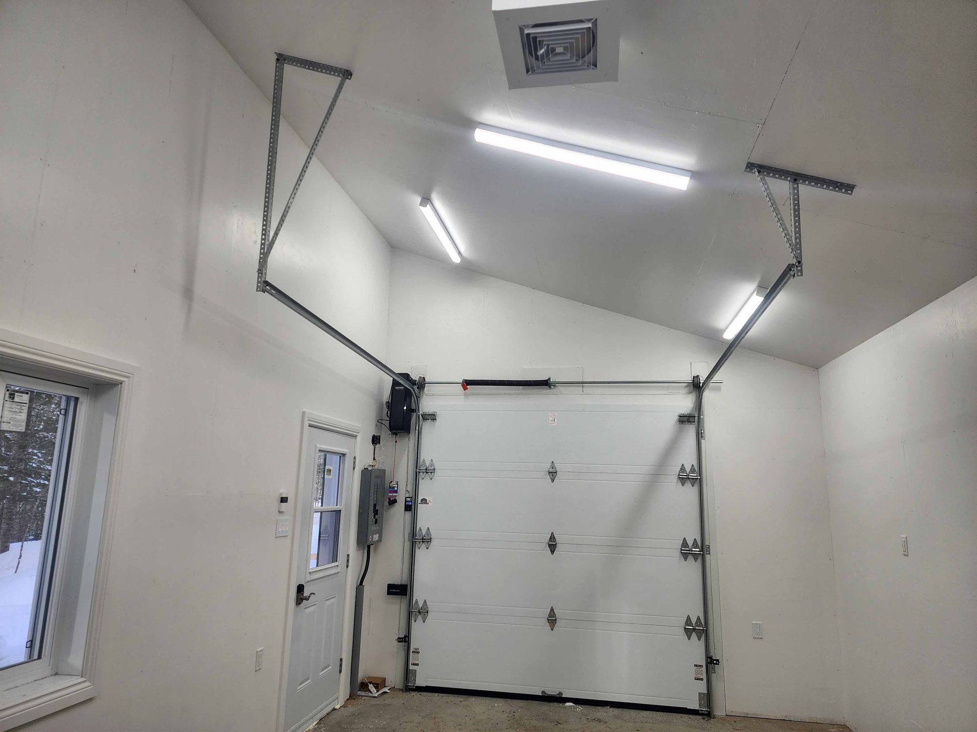 Intérieur de garage blanc avec porte sectionnelle fermée. Système de rails métalliques et éclairage installés au plafond.