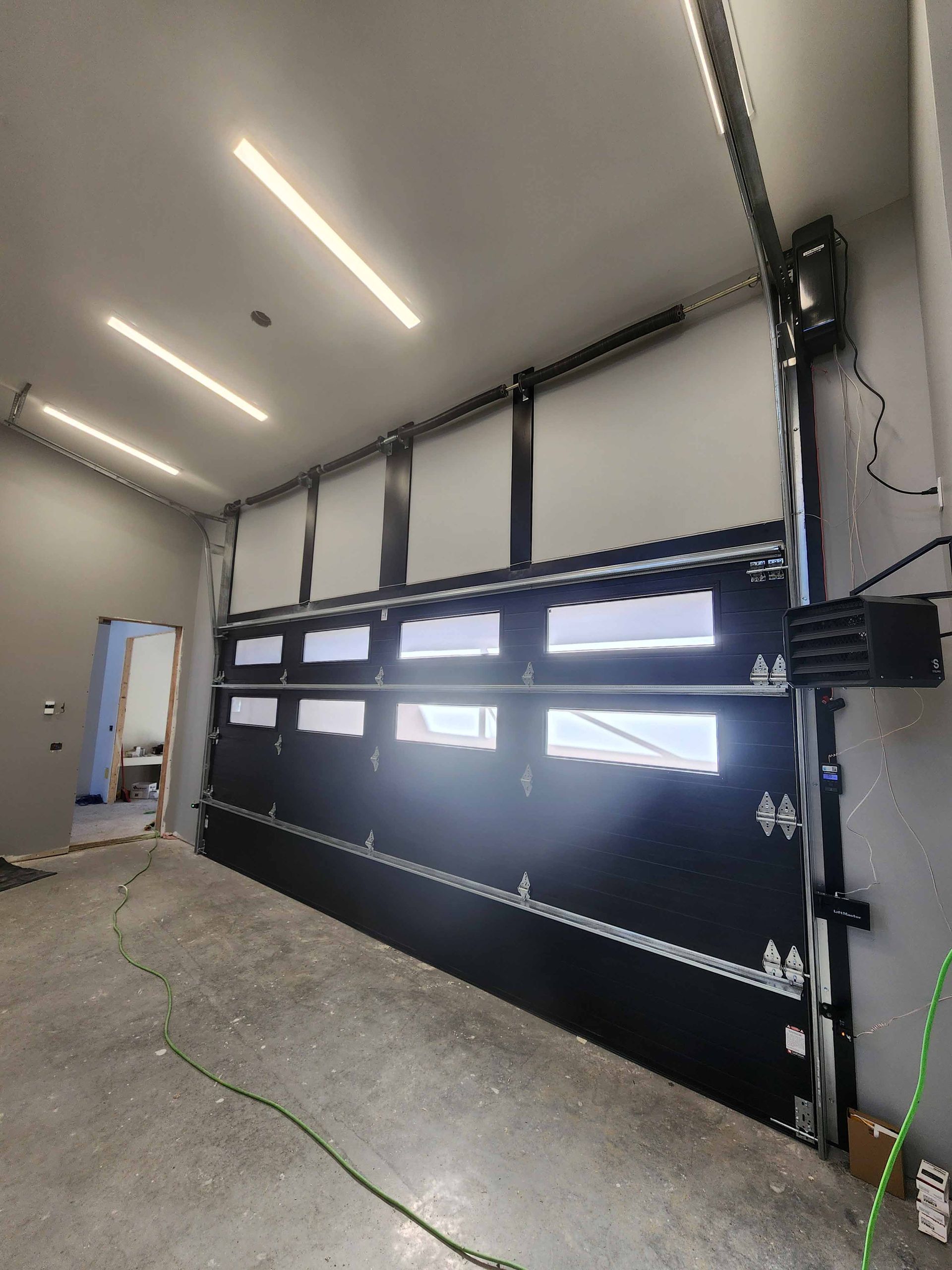 Porte de garage noire et blanche avec fenêtres, partiellement ouverte, à l'intérieur d'un garage en béton.