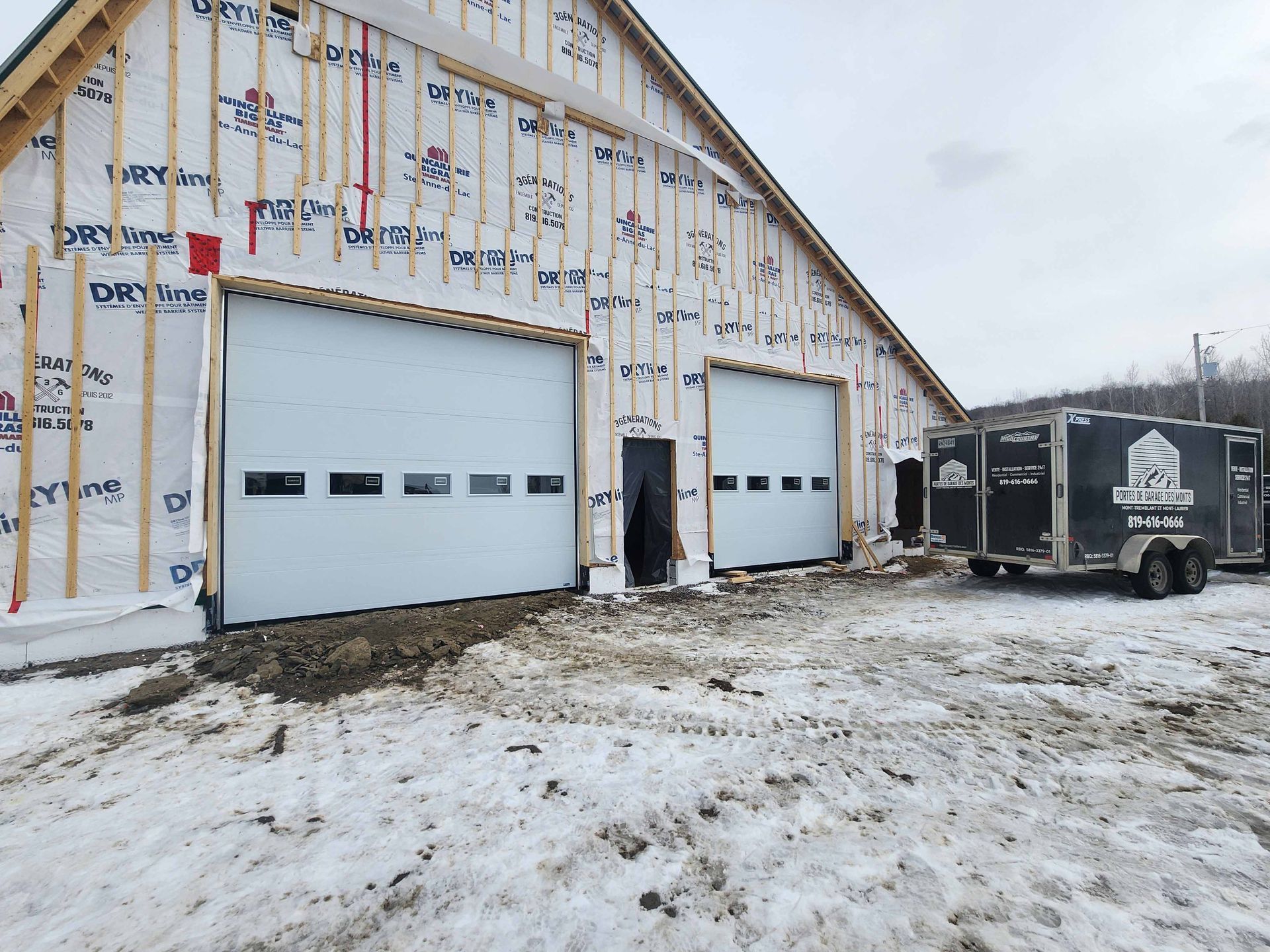 Vue intérieure d'un garage en construction, avec trois portes noires fermées. On aperçoit les câbles électriques jaunes.
