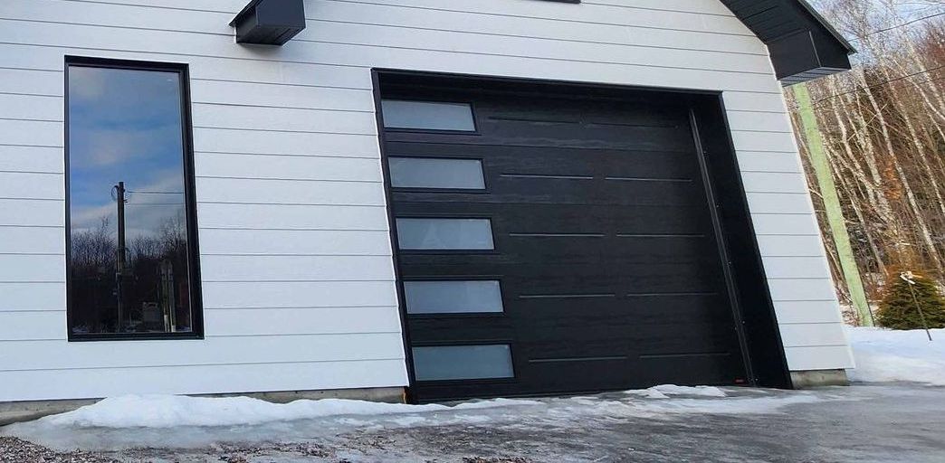 Porte de garage noire à vitres dépolies, installée dans un cadre en bois. Chantier, environnement extérieur.