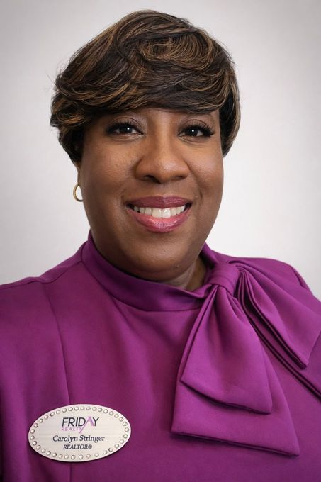 A person smiling while wearing a purple blouse with a neck tie and a name tag that reads