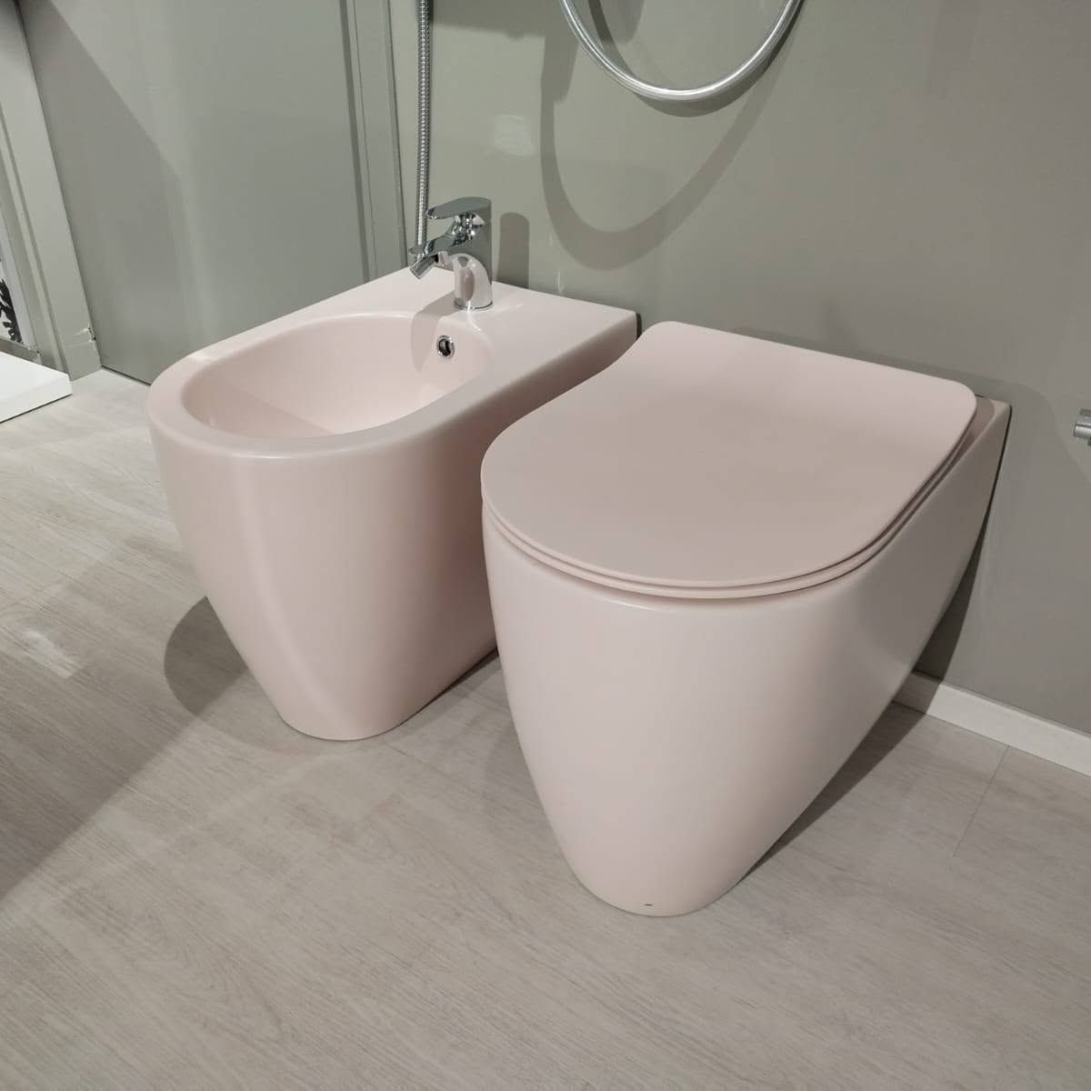 Lavabo e WC rosa moderni in un bagno minimalista con pareti grigie e pavimento chiaro.