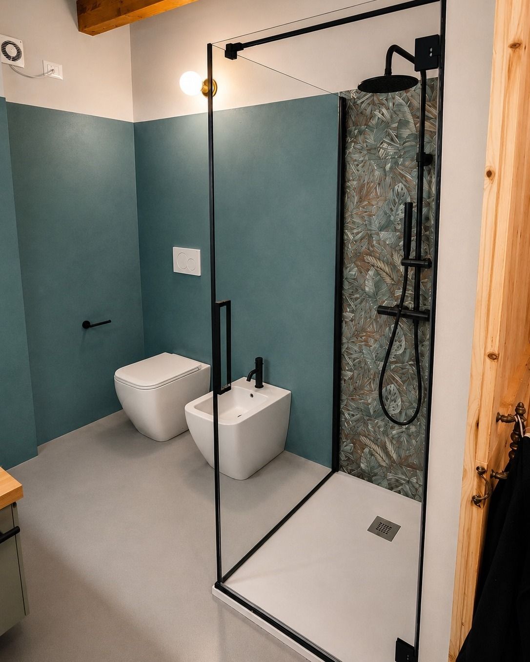 Bagno moderno con cabina doccia, pareti color verde acqua, sanitari bianchi e parete divisoria in vetro con cornice nera.