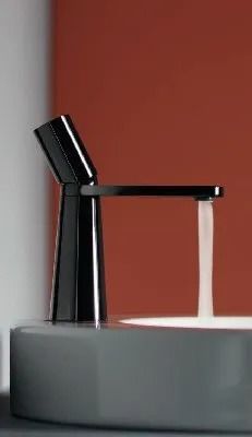 Rubinetto moderno nero con getto d'acqua bianca su un lavabo grigio, contro una parete color ruggine.