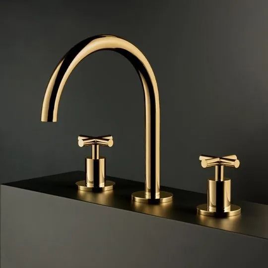Rubinetto dorato e due maniglie su un lavabo nero su sfondo scuro