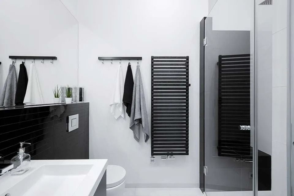 Bagno moderno in bianco e nero con lavabo, WC, portasciugamani e box doccia in vetro.