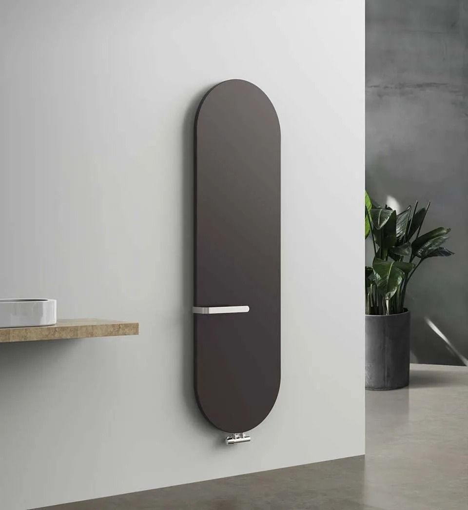 Radiatore ovale scuro a parete con asciugamano bianco in un bagno moderno e minimalista.