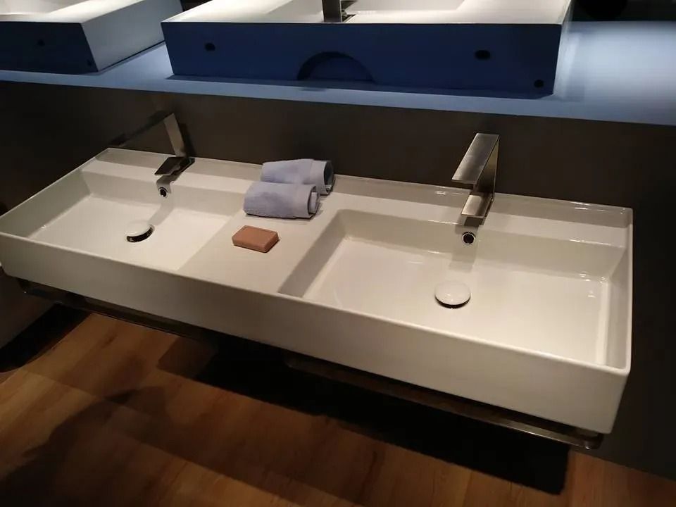 Mobile bagno moderno con due rubinetti cromati, lavabo bianco, asciugamani piegati e una saponetta.