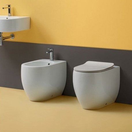 Bagno moderno con lavabo a parete e due WC bianchi su uno sfondo giallo e grigio.