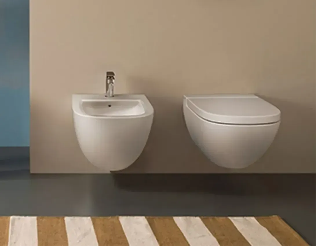 Lavabo bianco sospeso e WC a parete su una parete beige, sopra un tappeto a righe.