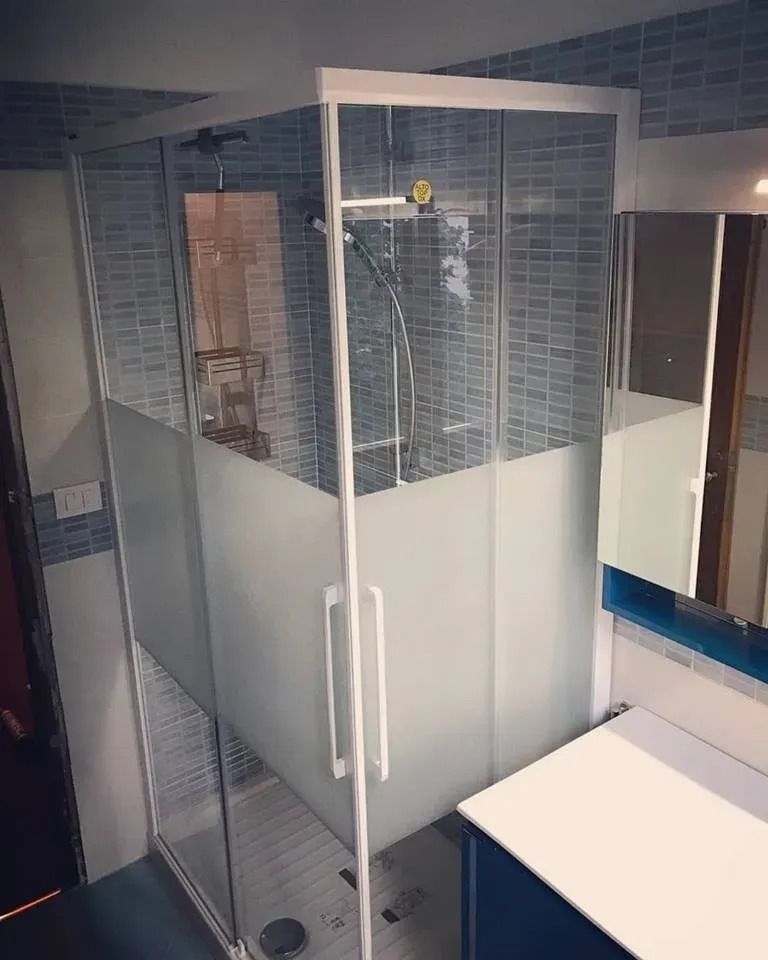 Box doccia in vetro con pannelli inferiori satinati e pareti del bagno rivestite in piastrelle.