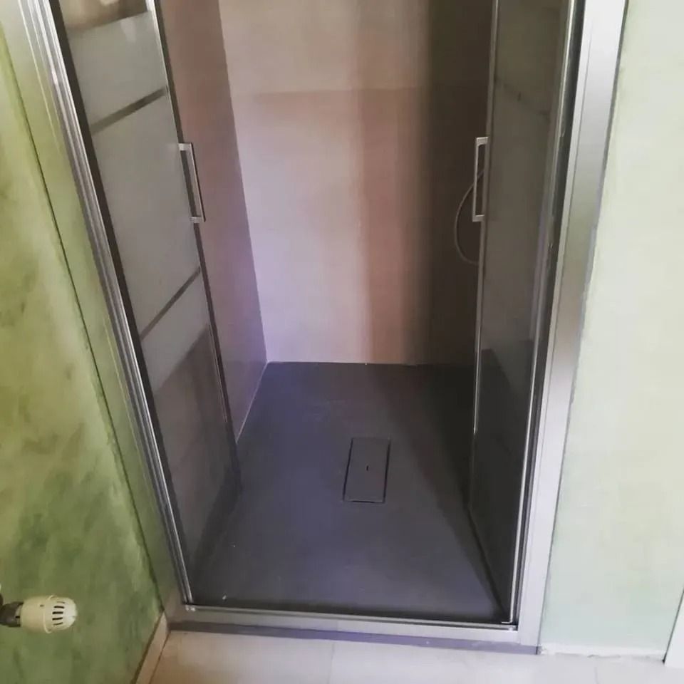 Si apre una porta su una piccola stanza vuota con pareti rosa e uno scarico a pavimento scuro.