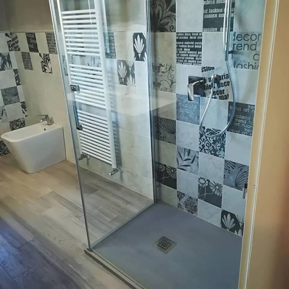 Bagno moderno con doccia in vetro, piastrelle grigie, opere d'arte alle pareti e vasca da bagno freestanding bianca.