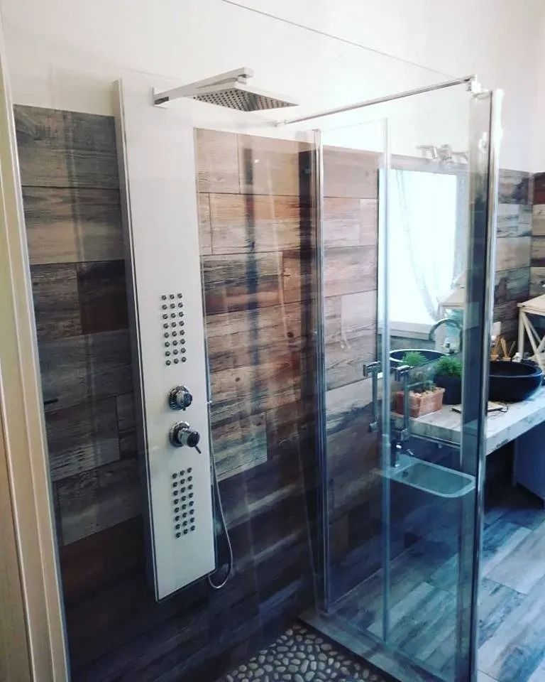 Bagno moderno con box doccia in vetro, pannelli a parete effetto legno e pannello di controllo doccia bianco.